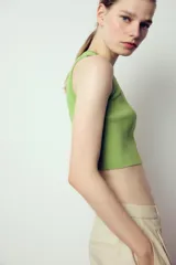 Top crop de tejido de punto color beige claro, con cuello redondo y manga sisa. Presenta acabados en rib en el cuello, sisas y bajo.