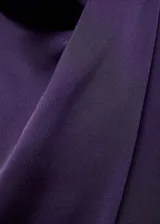 Blusa de tejido satinado color violeta, con cuello alto drapeado y mangas largas.