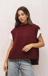 Chaleco tejido de punto en color bordó, con cuello alto y diseño de silueta amplia. Presenta aberturas laterales pronunciadas y un largo asimétrico, siendo más corto en la parte delantera y más largo en la espalda.