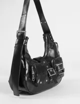 Cartera de hombro color marrón, confeccionada en cuero vegano con acabado brillante. Presenta un diseño estilo hobo con múltiples bolsillos frontales, uno con solapa y broches metálicos y otro con cierre, además de una hebilla central decorativa y herrajes plateados.