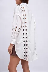 Camisa blanca de corte recto, con cuello clásico, cierre frontal con botones y mangas largas. Presenta apliques de encaje calado en los laterales del frente y en las mangas.