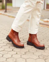 Botas cortas de cuero color marrón con suela track negra de goma. Presentan un diseño de corte clásico con paneles laterales texturizados y cierre lateral interno.