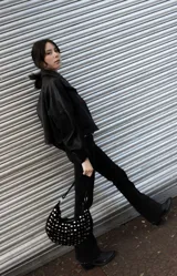 Bolso de hombro tipo hobo, color negro, con diseño de media luna y superficie completamente cubierta de tachas metálicas plateadas. Cuenta con asa corta para llevar al hombro y herrajes metálicos.