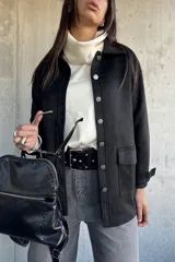 Chaqueta de gamuza negra con cierre frontal de botones metálicos, bolsillos laterales y cuello camisero.