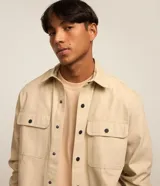 Camisa manga larga de sarga en color verde militar, con cuello inglés, cierre frontal de botones negros y dos bolsillos con solapa en el pecho.