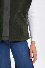 Chaleco de sherpa color verde con cuello alto y cierre frontal mediante botones a presión. Presenta una solapa central de tela técnica a tono y bolsillos laterales.