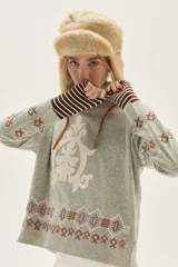 Polera de tejido de punto en color gris, con cuello alto y diseño holgado. Presenta un aplique central en color crema con motivos ornamentales y detalles bordados geométricos en la parte inferior y en las mangas.