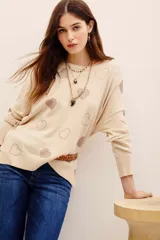 Sweater tejido de punto color beige con diseño holgado, cuello redondo, manga larga y aplicación de corazones formados con tachas brillantes en contraste.