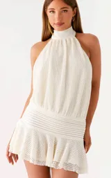 Vestido corto de tejido texturizado color blanco, con cuello halter alto, diseño sin mangas y falda con volados.