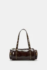 Bolso estilo bowling de cuero sintético acharolado color marrón, con diseño cilíndrico, bolsillos laterales con cierre y doble asa decorada con tachas metálicas doradas.