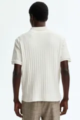 Remera polo de manga corta en punto texturizado de peso medio, color blanco, con cuello, tapeta de botones y bajo recto. Corte ajustado que realza el contorno del cuerpo.