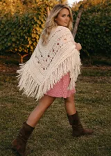 Ruana tejida en lana merino, con diseño calado y terminación de flecos largos en todo el contorno. Presenta una caída suave y envolvente.