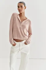 Sweater de punto color beige con cuello redondo, manga larga y cierre frontal parcial con botones. Presenta terminaciones en rib en cuello, puños y dobladillo.