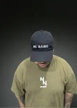 Gorro negro con visera curvada y bordado frontal con las palabras "NO BASIC" en color blanco.