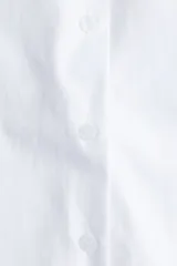 Camisa blanca de popelina de algodón, corte oversized con cuello clásico, hombros caídos y mangas largas con puños anchos abotonados. Presenta cierre frontal de botones y bajo redondeado.