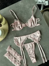 Conjunto de lencería de tres piezas color rosado, confeccionado en satén con detalles de encaje. Incluye soutiene con aro y copa armada, colaless y cinturón portaligas con tiras ajustables.