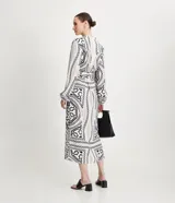 Vestido midi estilo chemise de satén con estampado de cadenas en blanco y negro. Tiene cuello redondo, mangas largas con puños elásticos, abotonadura frontal y cinturón con hebilla redonda.