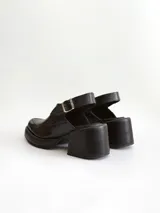 Zapato tipo slingback color negro, con plataforma y taco cuadrado. Presenta una puntera cuadrada y cierre con hebilla metálica en la tira trasera.