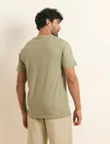 Remera básica de algodón color beige, de manga corta, con cuello redondo y un pequeño detalle bordado en el pecho.