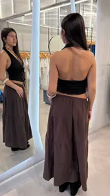 Top negro de textura gofrada, sin mangas y con escote halter. Cuenta con tiras ajustables con nudo en la parte frontal y abertura central.