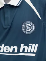 Camiseta tipo polo de manga corta con calce holgado, confeccionada en tejido técnico. Presenta cuello camisero en color blanco, detalles en contraste en hombros y mangas, y estampados gráficos en el frente con el logo de la marca y la inscripción golden hill.
