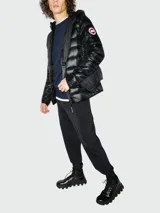 Campera puffer con capucha de plumas Canada Goose modelo Coftron, color gris brillante, con logo circular en el brazo y cierre frontal con cremallera. Incluye bolsillos laterales con cierre y correa bandolera con logo de la marca.