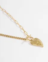 Collar de acero quirúrgico en tono dorado con cadena de diseño mixto, combinando eslabones finos y eslabones alargados. Presenta un cierre frontal tipo T-bar con un dije colgante en forma de corazón con detalle grabado.
