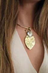 Gargantilla rígida dorada con dije colgante con forma de hoja martillada y piedra de nácar.