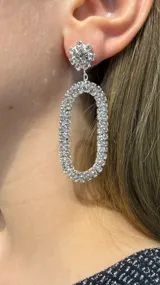 Caravanas colgantes de diseño ovalado, compuestas por una base circular con piedra central rodeada de cristales y un cuerpo en forma de óvalo completamente cubierto de strass brillante.