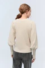 Sweater color crema de tejido de punto con lurex, mangas abullonadas y puños con botones metálicos.