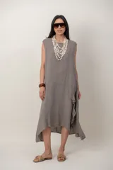 Vestido midi de lino color beige, sin mangas y con cuello redondo. Cuenta con un diseño irregular con detalle de volado vertical a un costado.