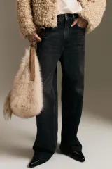 Jean de tiro alto con corte wide leg, confeccionado en denim rígido de color negro con efecto lavado. Presenta diseño clásico de cinco bolsillos, cierre frontal con cremallera y botón, y terminación de botamanga con ruedo desflecado.