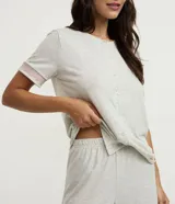 Pijama capri de viscolycra color gris melange, compuesto por una remera de manga corta con botonadura frontal y un pantalón capri. Ambas prendas cuentan con detalles de encaje rosado en las terminaciones.
