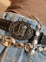 Cadena plateada para la cintura con eslabones de diferentes formas y tamaños. Incluye una cadena con eslabones ovalados y otra con dijes redondos con motivos florales.