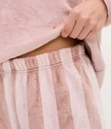 Pijama de dos piezas confeccionado en tejido fleece de tacto suave. La blusa es de cuello redondo y manga larga, con un pequeño bordado de flor en el pecho. El pantalón presenta un diseño de rayas verticales y cintura elástica.