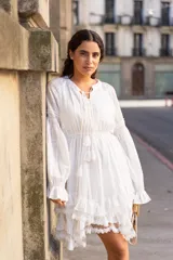 Vestido corto blanco de tela liviana con textura suave, escote en V con lazo, mangas largas amplias y volados en el ruedo.