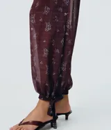 Pantalón largo estilo Aladino de Blue Steel, confeccionado en chiffon con estampado floral y detalles de encaje aplicado. Cuenta con cintura elástica y bajos ajustables con amarras en los tobillos.