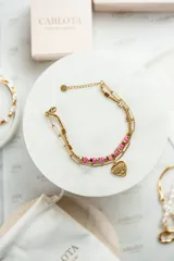 Pulsera dorada de acero quirúrgico con doble cadena, una de eslabones y otra con cuentas rosas. Dije en forma de corazón con ojo grabado y mini cristal.