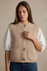 Chaleco de punto tejido color beige, con cuello redondo, cierre frontal de botones dorados grandes y bolsillos aplicados al frente.