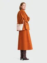 Bolso tipo bucket pequeño color rosa pálido, con asa corta y correa larga desmontable. Cierre superior con broche metálico dorado.