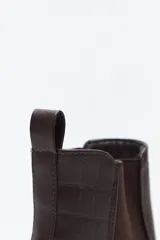 Bota tipo chelsea de caña baja con suela dentada robusta. Presenta un diseño combinado con paneles laterales elásticos, acabado liso en el frente y detalle texturizado en relieve en la parte posterior, incluyendo un tirador trasero para facilitar el calce.