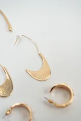 Set de tres pares de caravanas doradas de diferentes diseños: un par de aros alargados y curvos, un par de aros con dije en forma de media luna texturizada y un par de aros tipo argolla pequeña.