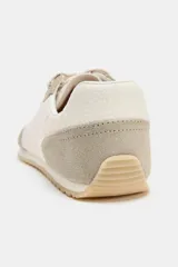 Zapatillas deportivas estilo barefoot con puntera amplia y suela plana flexible. Presentan un diseño combinado en tonos beige y crema, con paneles de gamuza y tela, cierre mediante cordones bicolor y suela con efecto engomado.