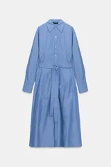Vestido midi de estilo camisero con cuello solapa, manga larga con puños y cierre frontal con botones. Presenta un diseño a rayas verticales, bolsillos laterales ocultos y un cinturón de lazada en el mismo tejido para ajustar a la cintura.