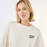 Camiseta de corte oversize color blanco crudo, con cuello redondo y mangas cortas. Presenta un pequeño estampado tipográfico en el pecho con la frase 'East Side League'.