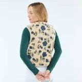 Chaleco sin mangas confeccionado en tejido tipo corderito, con estampado floral en tonos azules y verdes sobre base beige. Presenta escote en V, cierre frontal con botones a presión y ribetes en color crema.
