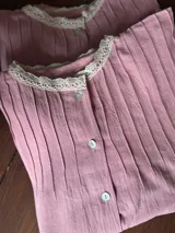 Camisa rosa viejo con diseño plisado vertical, cuello redondo adornado con puntilla beige y cierre frontal de botones nacarados.