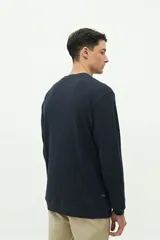 Buzo de felpa gris oscuro, con textura de tejido waffle o gofrado. Presenta cuello redondo, manga larga y un pequeño logo bordado en el pecho.