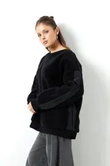 Buzo negro de tela tipo teddy, de manga larga y cuello redondo. Presenta recortes de nylon en mangas y laterales.