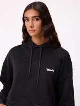 Canguro oversize color negro con efecto lavado, capucha y estampa gráfica en la espalda con tipografía desgastada y detalles en color turquesa.